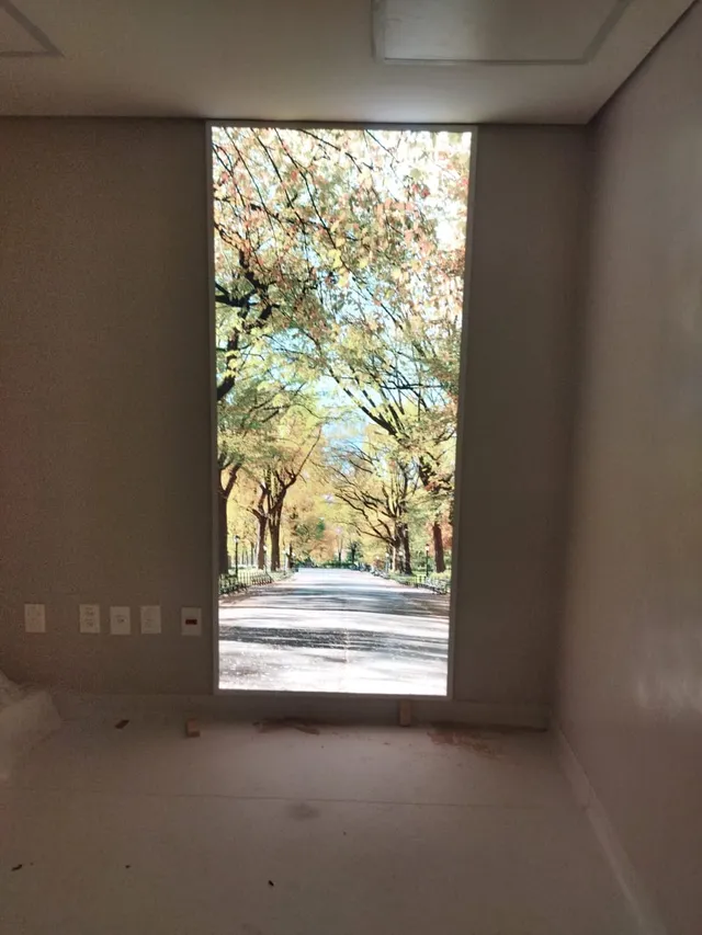 Painel iluminado simulando janela com paisagem de parque em ambiente fechado